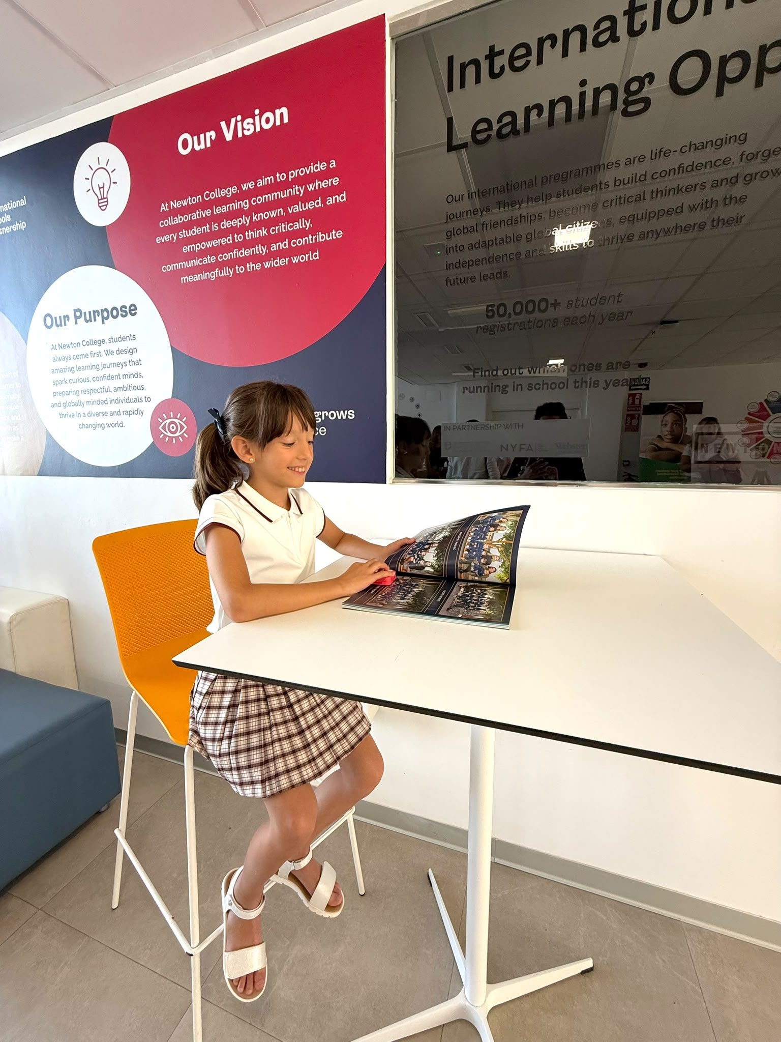 Catinca răsfoind broșura școlii, lângă panoul Our Vision de la Colegiul Newton